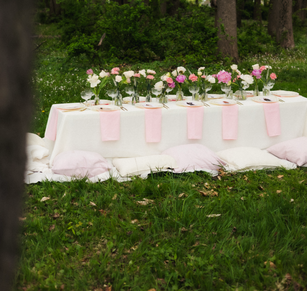 Outdoor low table setup with white linen, pink napkins, and pastel floral arrangements on grass