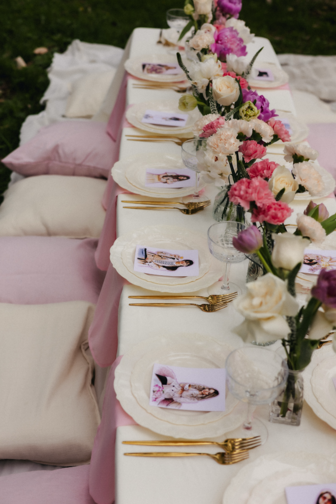 Long low table with floor cushions, pink florals, gold cutlery, and photo place cards for garden party