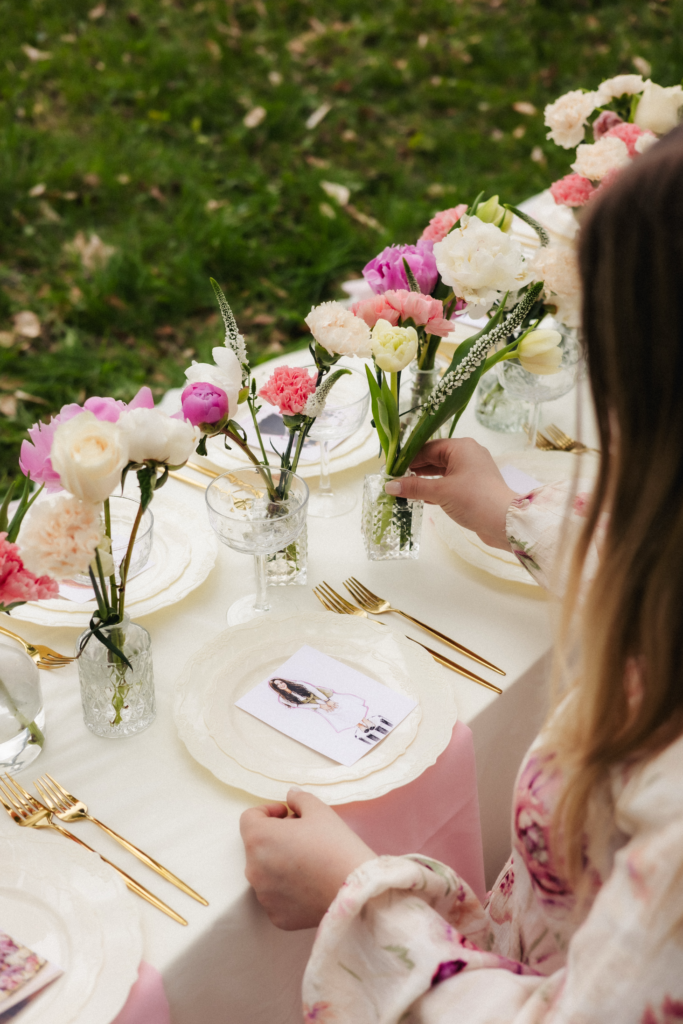 Event stylist arranging flowers on outdoor birthday table with white plates and personalized place cards