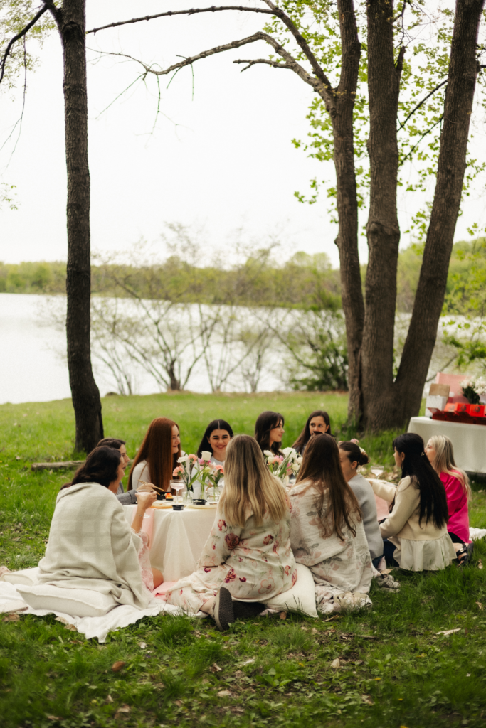 Group of women sitting around low outdoor table at enchanted garden birthday celebration by the lake