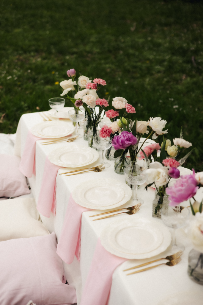 Garden birthday tablescape with pink and white peony arrangements in glass vases and gold flatware