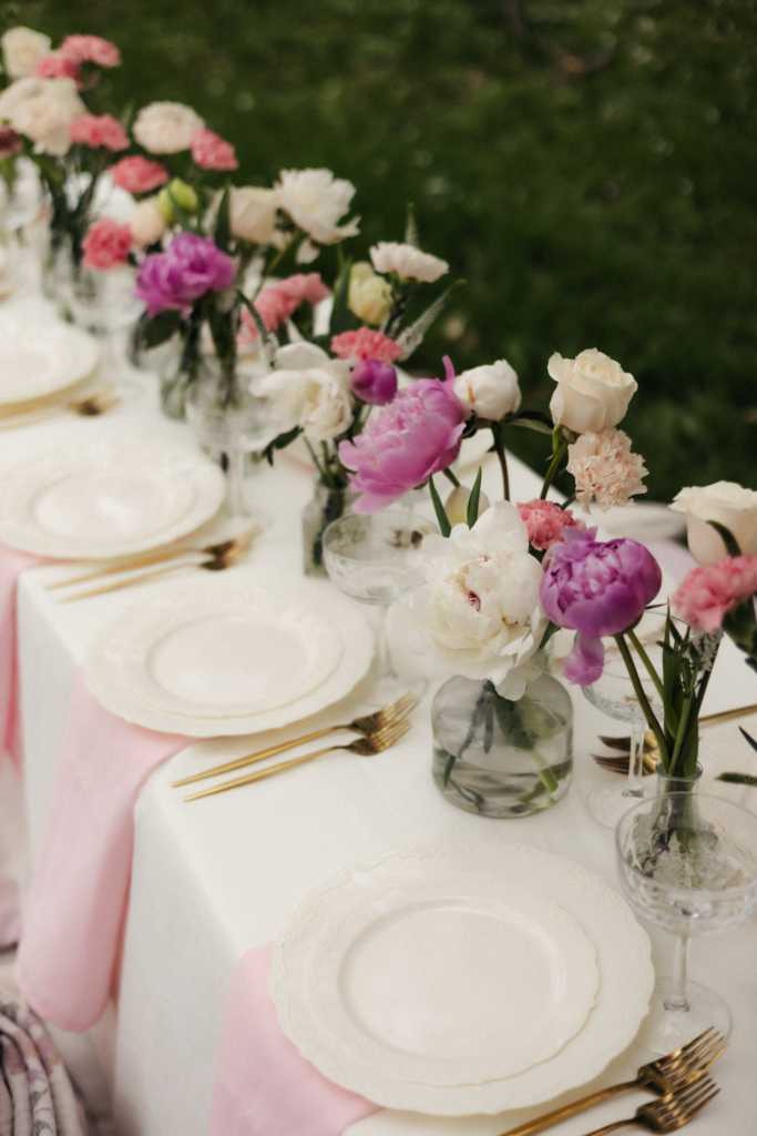 Garden birthday tablescape with pink and white peony arrangements in glass vases and gold flatware