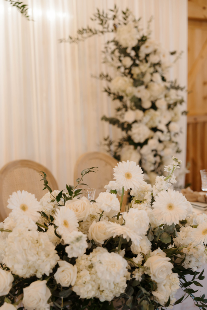 Lush white floral arrangement with dahlias, roses, and greenery for luxury wedding decor